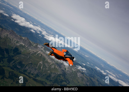 Paracadutista è volare entro la sua wingsuit arancione su un paesaggio spettacolare. Il subacqueo è il percorso lungo il crinale. Foto Stock