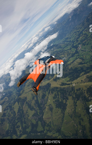 Paracadutista è volare entro la sua wingsuit arancione su un paesaggio spettacolare. Il subacqueo è il percorso lungo il crinale. Foto Stock