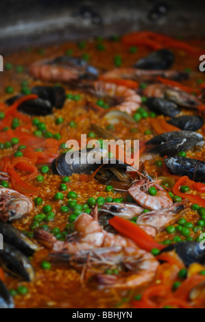 La paella nel tegame grande lentamente la cottura in un salone del cibo. Questo piatto spagnolo include: pollo, peperoni, riso, gamberi e altri frutti di mare. Foto Stock