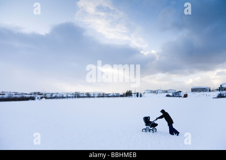 Una donna che cammina con una carrozzina nella neve. Hafnarfjordur, una maggiore area di Reykjavik, Islanda Foto Stock