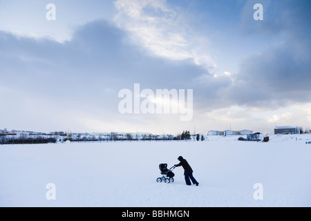 Una donna che cammina con una carrozzina nella neve. Hafnarfjordur, una maggiore area di Reykjavik, Islanda Foto Stock