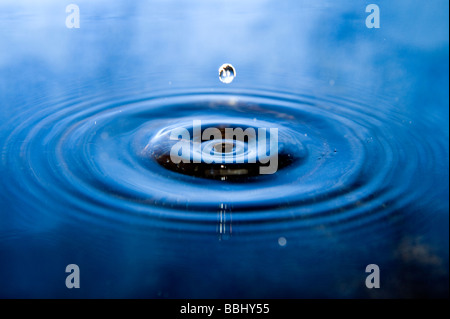 Singola goccia che cade in acqua. Il cielo che riflette in superficie. Foto Stock