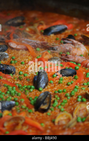 La paella nel tegame grande lentamente la cottura in un salone del cibo. Questo piatto spagnolo include: pollo, peperoni, riso, gamberi e altri frutti di mare. Foto Stock