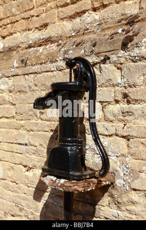 Una ghisa nera pompa acqua su un vecchio muro di pietra Foto Stock