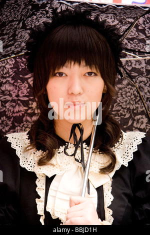 Tokyo, Harajuku. Cosplay. Primo piano ritratto della giovane donna giapponese in classico gotico Lolita abbigliamento con ombrello, posa guardando spettatore. Foto Stock