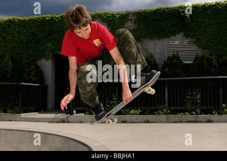 Airborne boy facendo un mute grab slobair su uno skateboard al di sopra di un recipiente di cemento a Toronto il parco all'aperto Foto Stock