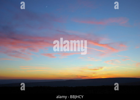 Di rosso le nuvole e la luna crescente in un crepuscolo blu cielo sopra una silhouette di Pennine colline, a ovest di Halifax, Regno Unito Foto Stock