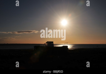 Sun silhouette di una barca da pesca ormeggiate sulle sabbie in corrispondenza del bordo del Ribble Estuary a Lytham, vicino a Blackpool, Lancashire, Regno Unito Foto Stock