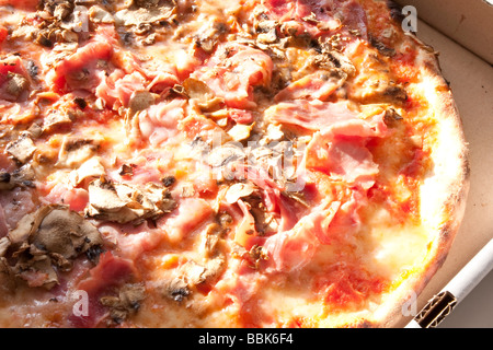 Pizza appena sfornata con prosciutto e funghi, luccicante con formaggio fuso. Foto Stock