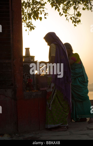 Le donne indiane a pregare e a rendere offrendo sotto un albero sacro, durante un rituale mattutino. Assi la balneazione ghat sul fiume Gange. Foto Stock