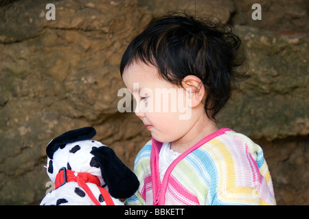 Un giovane semi-Thai bambina guarda al suo soffice, macchie cane giocattolo sotto un uomo arco di roccia a Skegness promenade, Lincolnshire Foto Stock