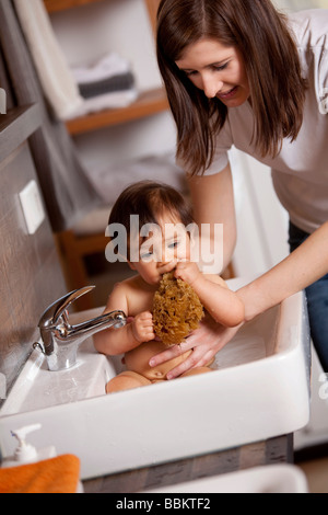 Nove-mese-vecchio baby è mordere in una spugna pur essendo immerso nel lavandino Foto Stock