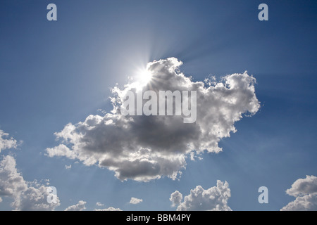 Sun dietro una nuvola bianca di fronte a un cielo blu Foto Stock