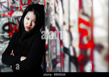 Giovane ragazza asiatica appoggiata contro un muro di graffiti nel rapper-style Foto Stock