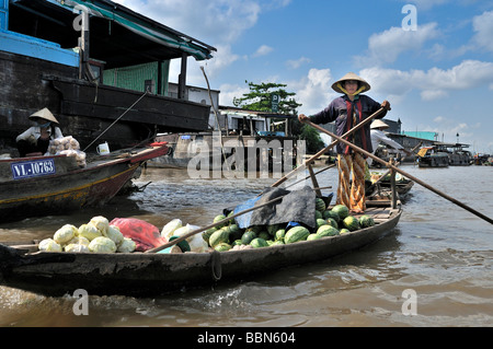 Donna con cappello tradizionale a forma di cono hat fatte di foglie di palma, permanente e la barca a remi di una barca di legno sul Mekong, carico di frutta Foto Stock