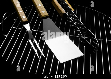 Tre in acciaio inox utensili da barbecue sul grill. Forcella, spatola, tenaglie. Studio shot su sfondo nero. Foto Stock