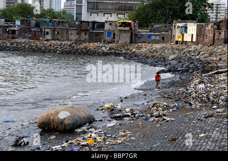 Ragazzo walknig lungo una immondizia disseminata beach in Mumbai, India Foto Stock