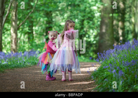 Due giovani bambini vestiti come fate esplorare bluebell riempito bosco in Inghilterra. Foto Stock