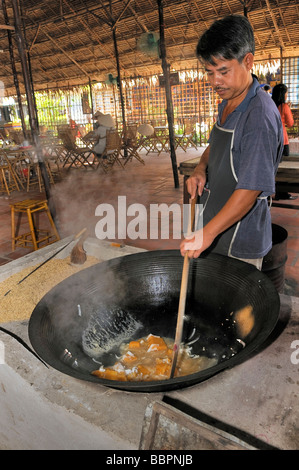 L'uomo sotto agitazione in un recipiente di metallo durante la preparazione di riso soffiato dolci, pasticceria fabbrica, Vinh Long, Delta del Mekong, Vietnam, Sud Foto Stock