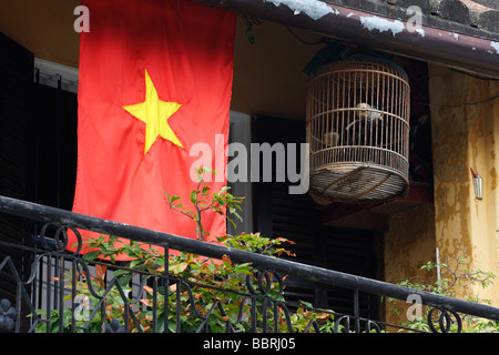 Nazionale vietnamita bandiera rossa e la birdcage sospesi dal balcone della casa, "Hoi An', Vietnam Foto Stock