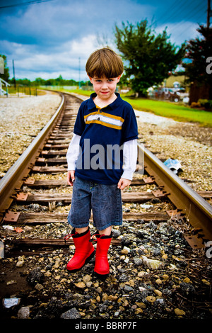 Ragazzo sui binari del treno con stivali rossi Foto Stock