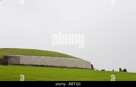 In attesa del prossimo tour di Newgrange. Una guida turistica con un ombrello blu sorge accanto alla vasta parete e il tumulo di Newgrange. Foto Stock