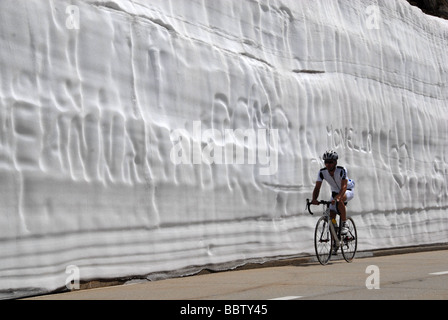 Equitazione Bicycler sotto un enorme muro di neve in primavera su Nufenen pass road alpi svizzere Svizzera Foto Stock