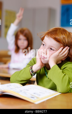 I bambini in una classe della scuola primaria, ragazzo fantasticando o cercando certi, meditata, triste o frustrato, ragazzi diventando il Foto Stock