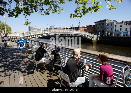 Persone in cafe sul fiume Liffey boardwalk sulla parte inferiore Ormond Quay con vista al Ha Penny bridge centrale di Dublino Repubblica di Irlanda Foto Stock