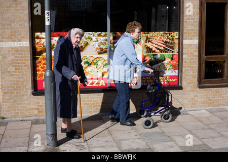 Anziane signore di camminare con attenzione lungo la strada di fronte a pizza da asporto shop in Weston-Super-Mare. Foto Stock