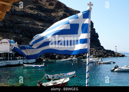 Bandiera Greca a Ammoudi - vicino a Oia con barche da pesca in background Foto Stock