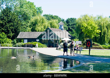 Londra , Regent's Park , scena pacifica dei bambini sul lago in barca con due oche canadesi & cafe ristorante in background Foto Stock