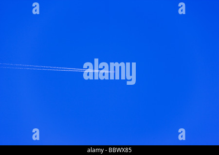 Volo aereo di linea in altitudine, cielo blu chiaro con contrails. Foto Stock