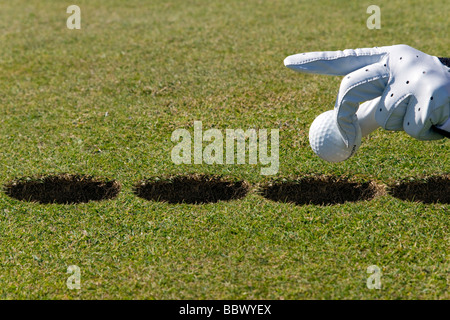 Mano che tiene la pallina da golf su diversi fori, l'altra sorta di messa Foto Stock