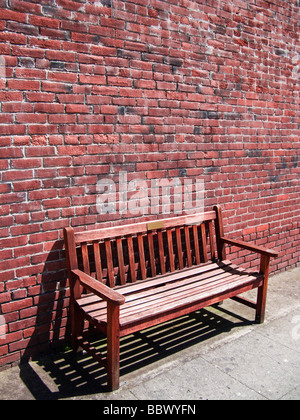 Una panca in legno si siede di fronte a un muro di mattoni. Foto Stock