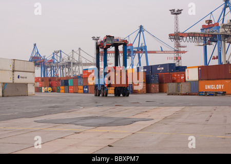 Un "straddle carrier carrello si sposta i contenitori ISO intorno al contenitore terminale per essere impilati e trasformati. Foto Stock