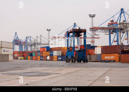 Un "straddle carrier carrello si sposta i contenitori ISO intorno al contenitore terminale per essere impilati e trasformati. Foto Stock