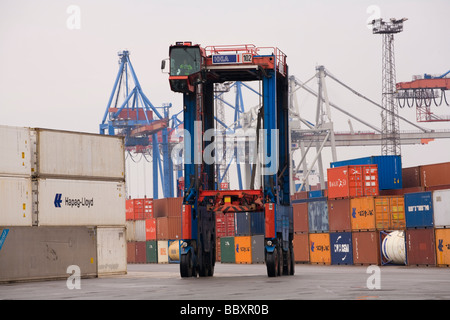 Un "straddle carrier carrello si sposta i contenitori ISO intorno al contenitore terminale per essere impilati e trasformati. Foto Stock