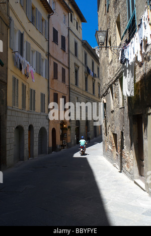 Uomo che cavalca scooter lungo la strada stretta a Siena, Italia Foto Stock