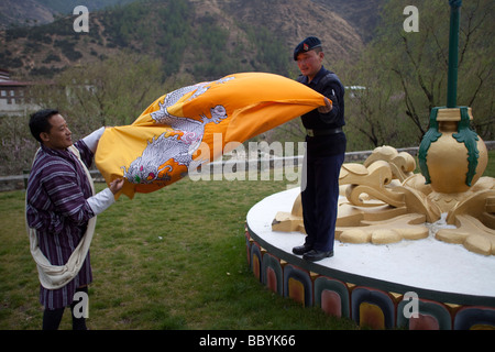 Soldato bhutanesi guard ripiegamento Bhutan bandiera nazionale al palazzo del re, Thimphu. Visualizzazione orizzontale Foto Stock