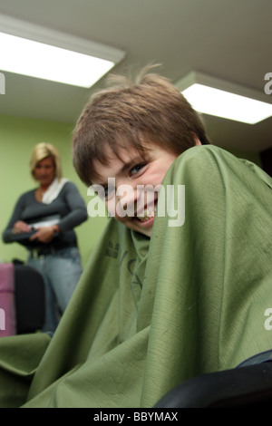 Sorridente ragazzo seduto nella sedia di stilisti prima di ottenere un taglio di capelli Foto Stock