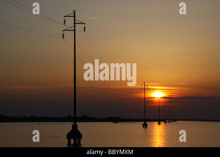 Tramonto e stagliano i cavi di alimentazione dai piloni, fornendo albarella island, Italia Foto Stock