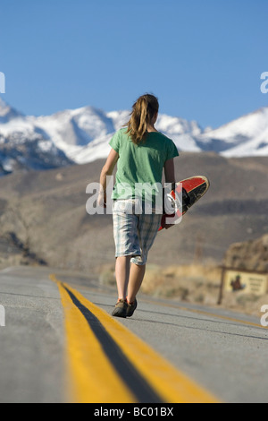 Giovane donna skateboarding in Vescovo, CA con le montagne sullo sfondo. Foto Stock