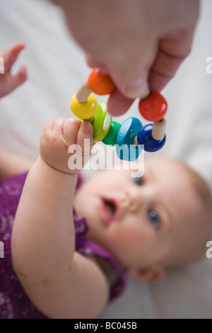Tre mesi di età bambina di raggiungere per un legno giocattolo per la dentizione Foto Stock