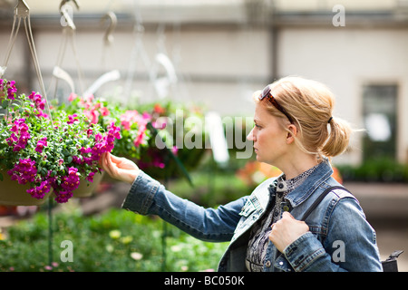 Donna che guarda cesti floreali pendenti in una serra. Foto Stock