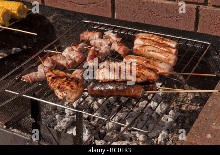 Close-up di salsicce, hamburger e grano e spiedini cucinati all aria aperta su un barbecue (barbecue) in estate Foto Stock