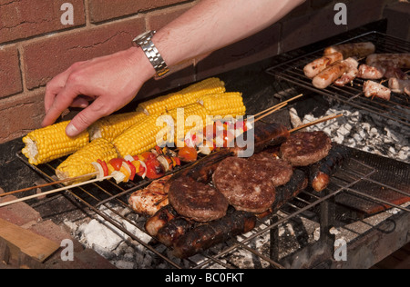 Close-up di salsicce, hamburger e grano e spiedini cucinati all aria aperta su un barbecue (barbecue) in estate Foto Stock