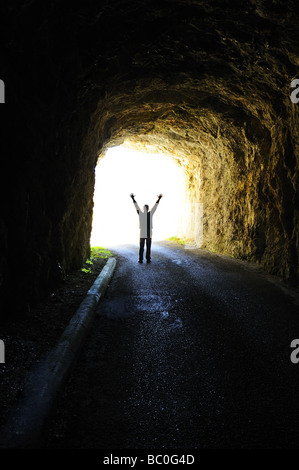 La luce alla fine del tunnel. Silhouette di una figura in piedi alla fine di un tunnel buio guardando fuori in presenza di luce solare intensa. Foto Stock