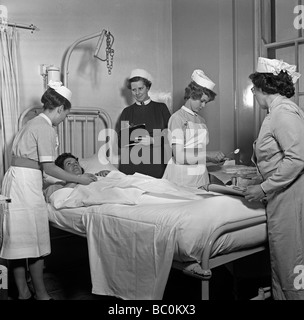 Infermieri e matrona riuniti intorno a un paziente in ospedale, c. 1960 Foto Stock