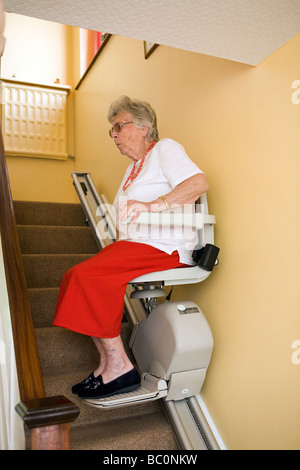 Una vecchia signora utilizza una sedia di sollevamento per spostare su e giù per le scale di casa sua Foto Stock